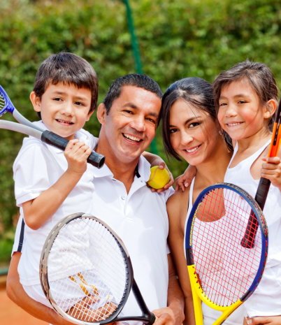 A man and woman are holding a little boy and little girl. The family has been playing tennis.