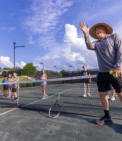 A male tennis pro instructs young players on the court.